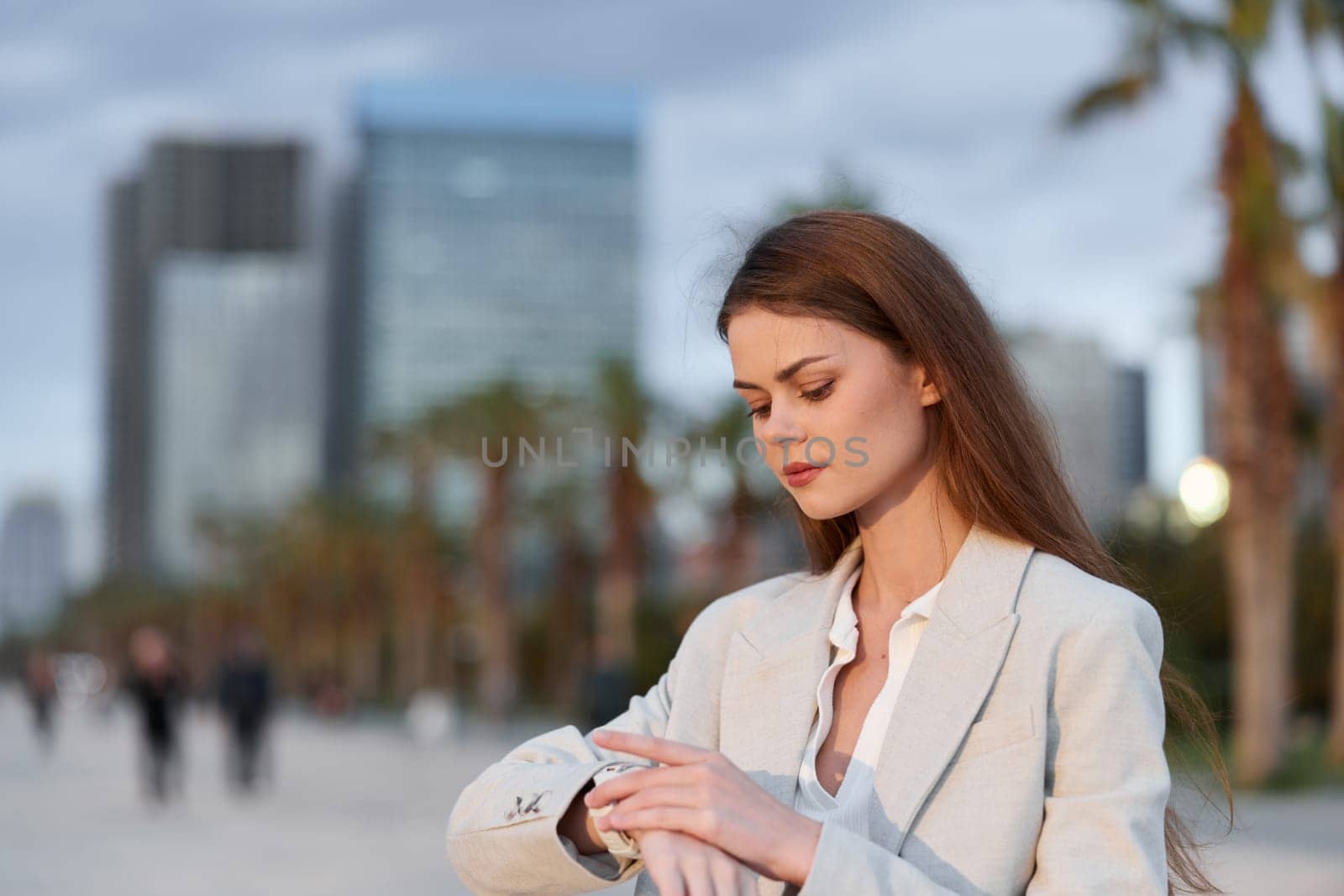 A focused business woman in a stylish suit looks at her watch against a modern city backdrop. Her confident demeanor reflects professionalism and determination, ideal for corporate themes.