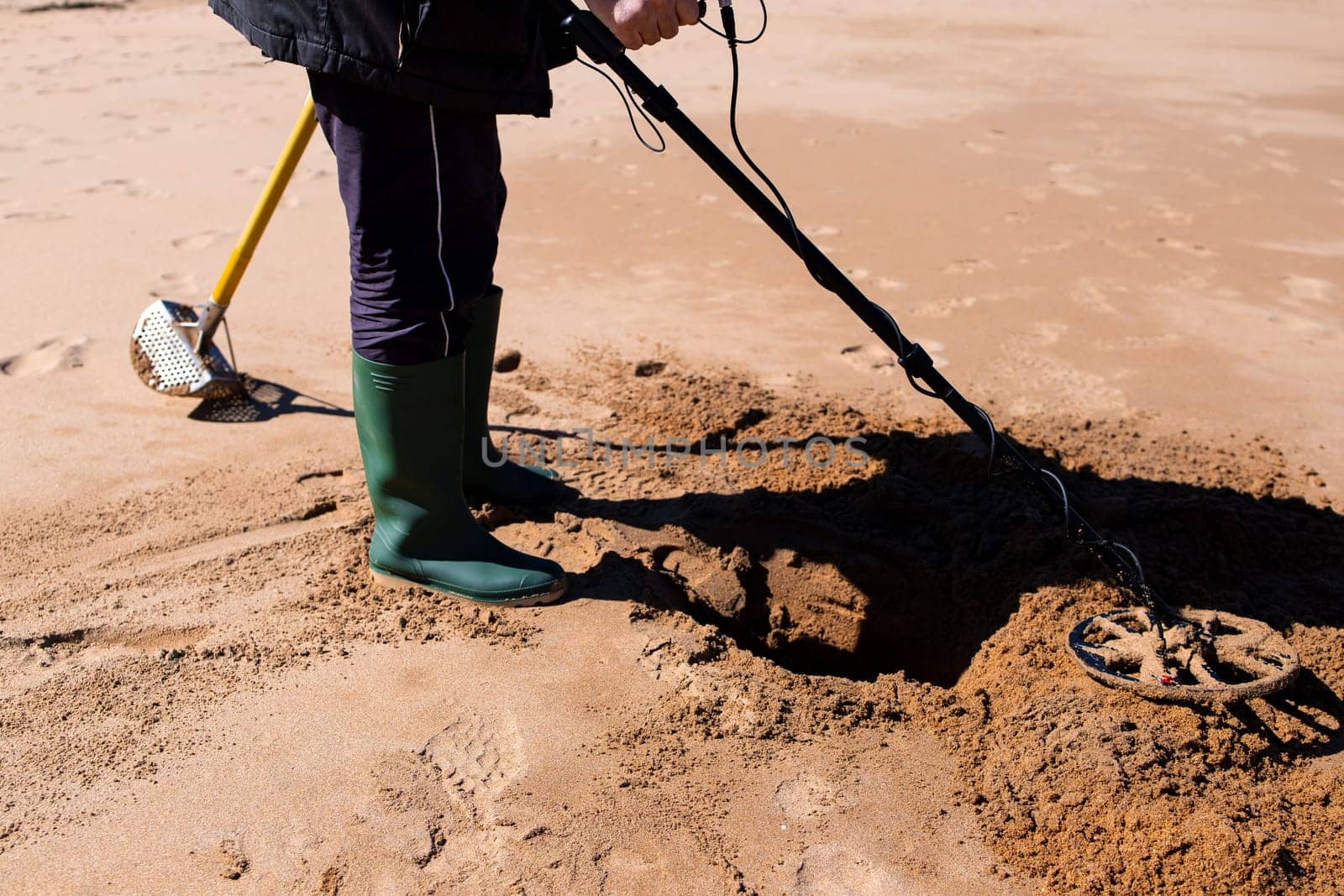 Person using metal detector on sandy beach for buried treasures.