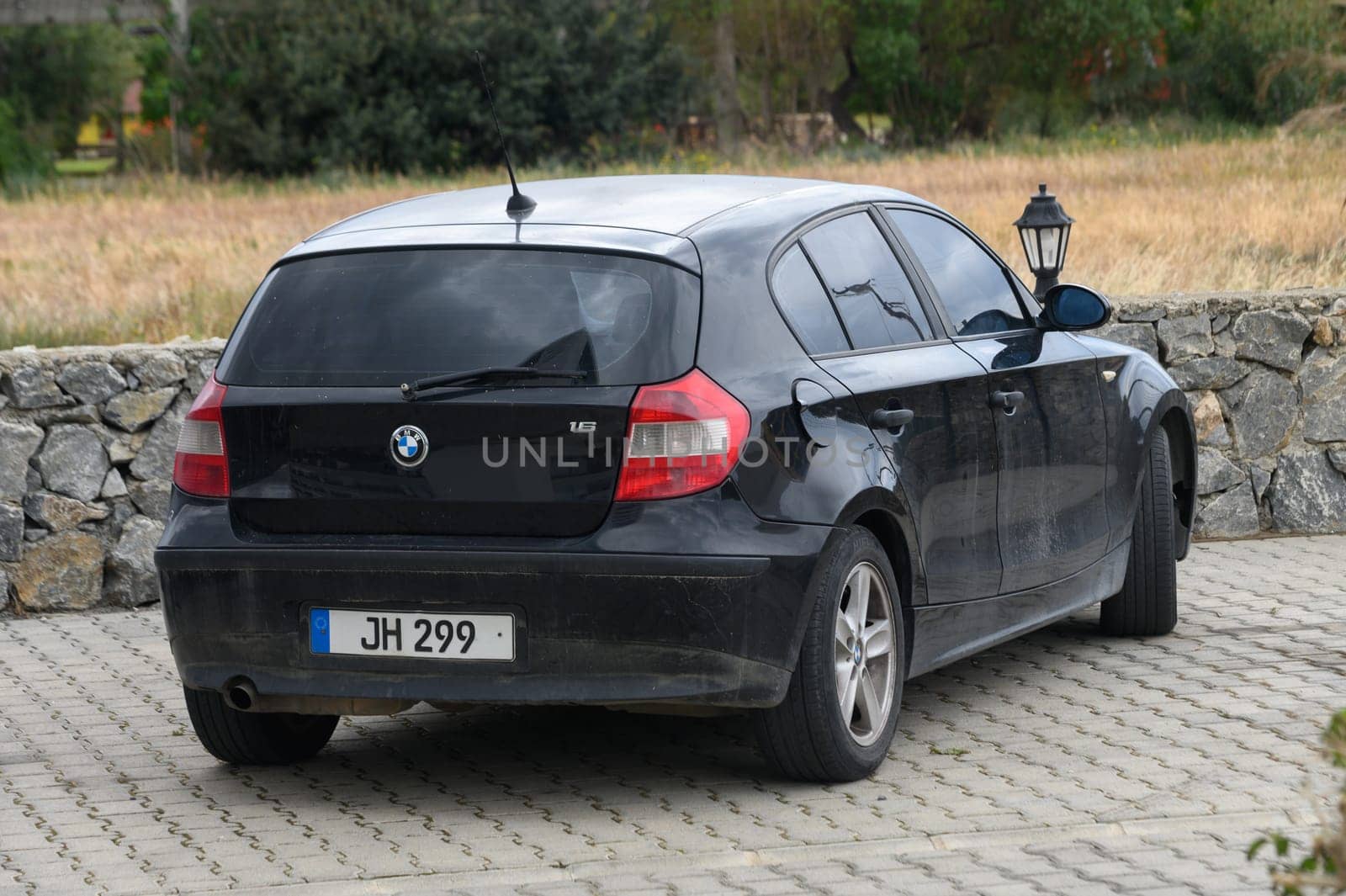 Gaziveren Cyprus -10.04.2025 A sleek black hatchback is parked on a stone driveway, blending with the rustic charm of the countryside. Golden fields stretch beyond, creating a serene and peaceful atmosphere.
