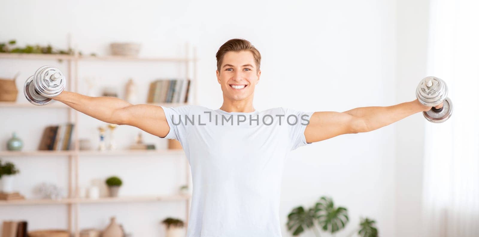 Healthy lifestyle and strength training. Strong man raises dumbbells in interior of living room, free space