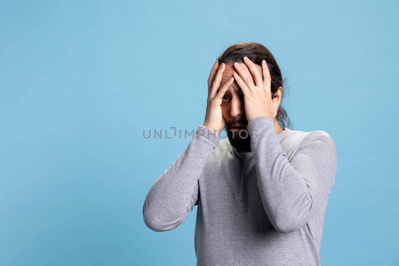 Horrified young guy in shock getting really scared and worried about something, being distraught and fearful against blue background. Afraid terrified man being frightened, horror reaction.