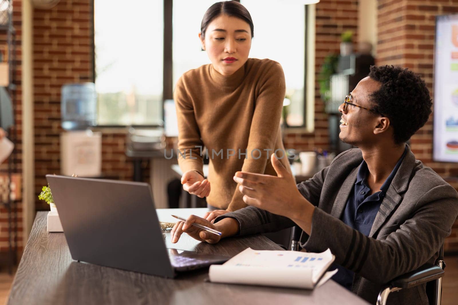 Male business analyst pointing at laptop and explaining strategy improvements to attentive coworker. Diverse colleagues checking financial reports, ensuring accuracy in business performance metrics.