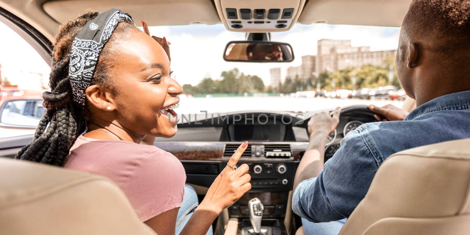 Back view of happy black lovers sitting in nice car, going vacation together by car. Cheerful african american millennial man and woman enjoying trip, having conversation, laughing