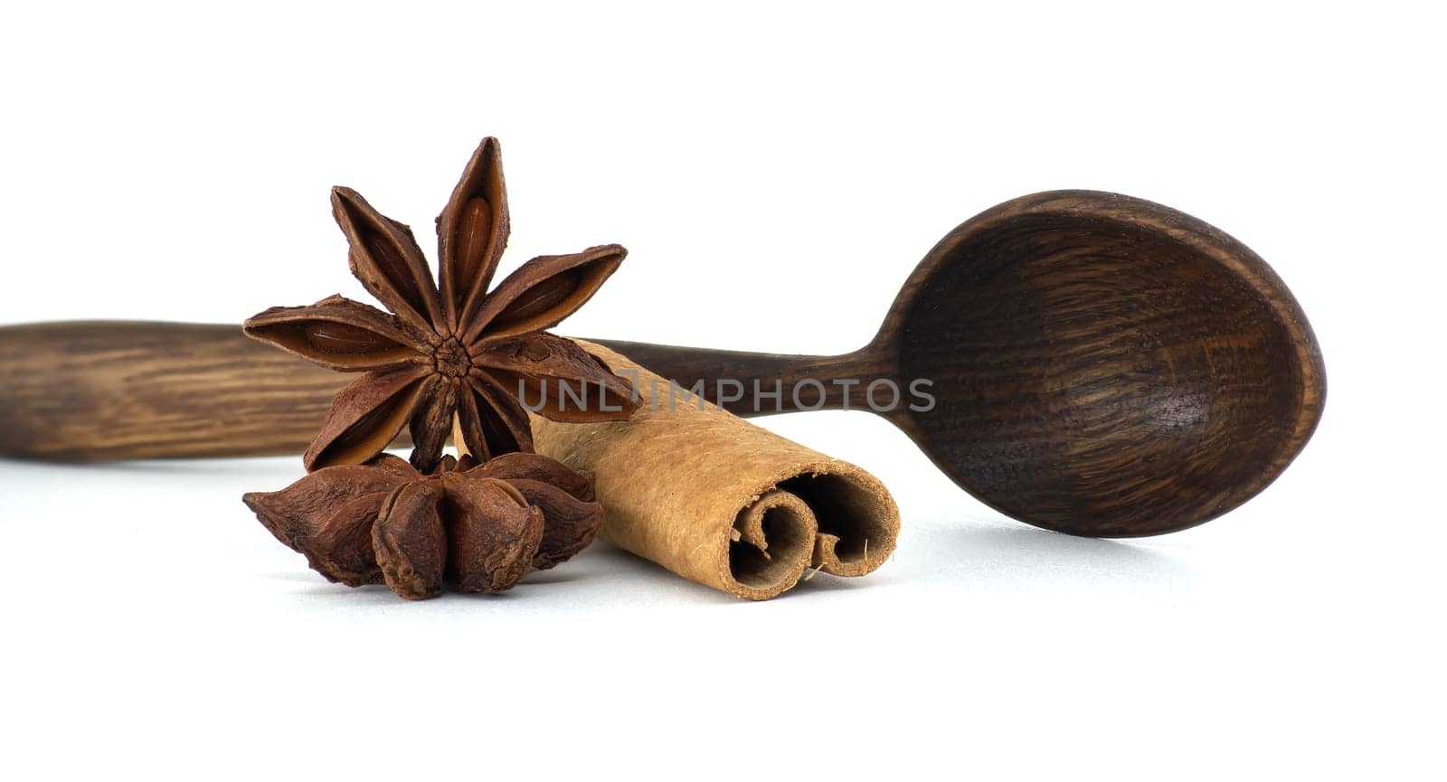 Aromatic star anise and a cinnamon stick rest next to a rustic wooden spoon on a clean, white surface, capturing a sense of culinary warmth.
