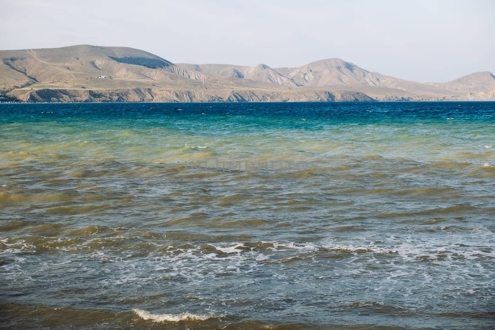 Polluted sea washing Crimean coast with brown waves and mountains in the background
