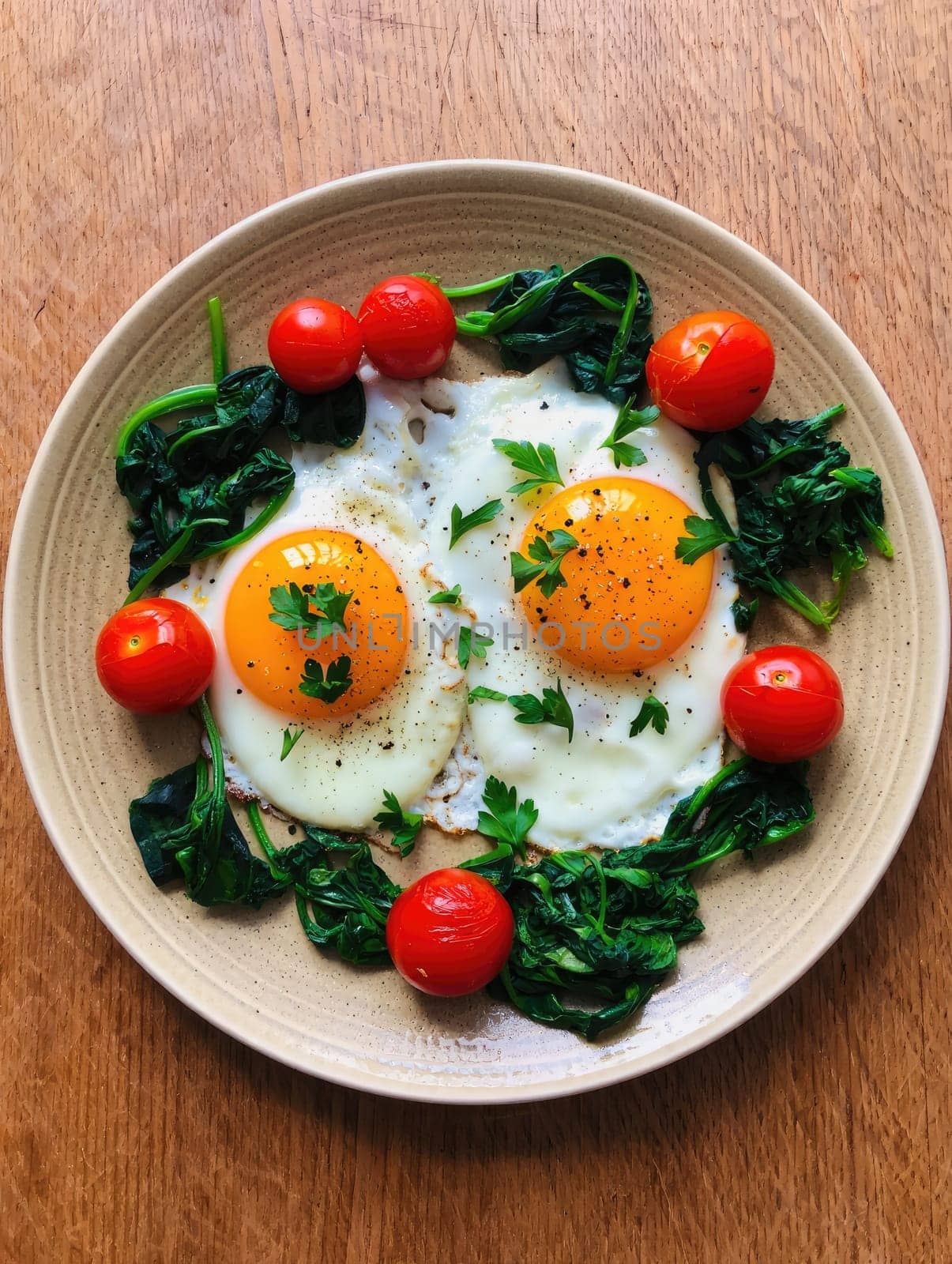 Two sunny side up eggs are placed on a bed of sautéed spinach with cherry tomatoes surrounding them. Fresh parsley adds a touch of color to this nutritious breakfast dish.