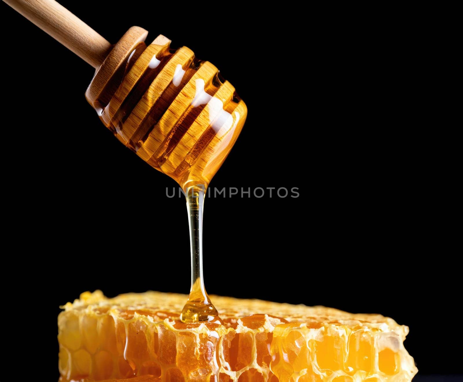 A wooden dipper drips golden honey over a fresh honeycomb piece. The dark background highlights the rich color and texture of the honey, creating a visually appealing contrast.