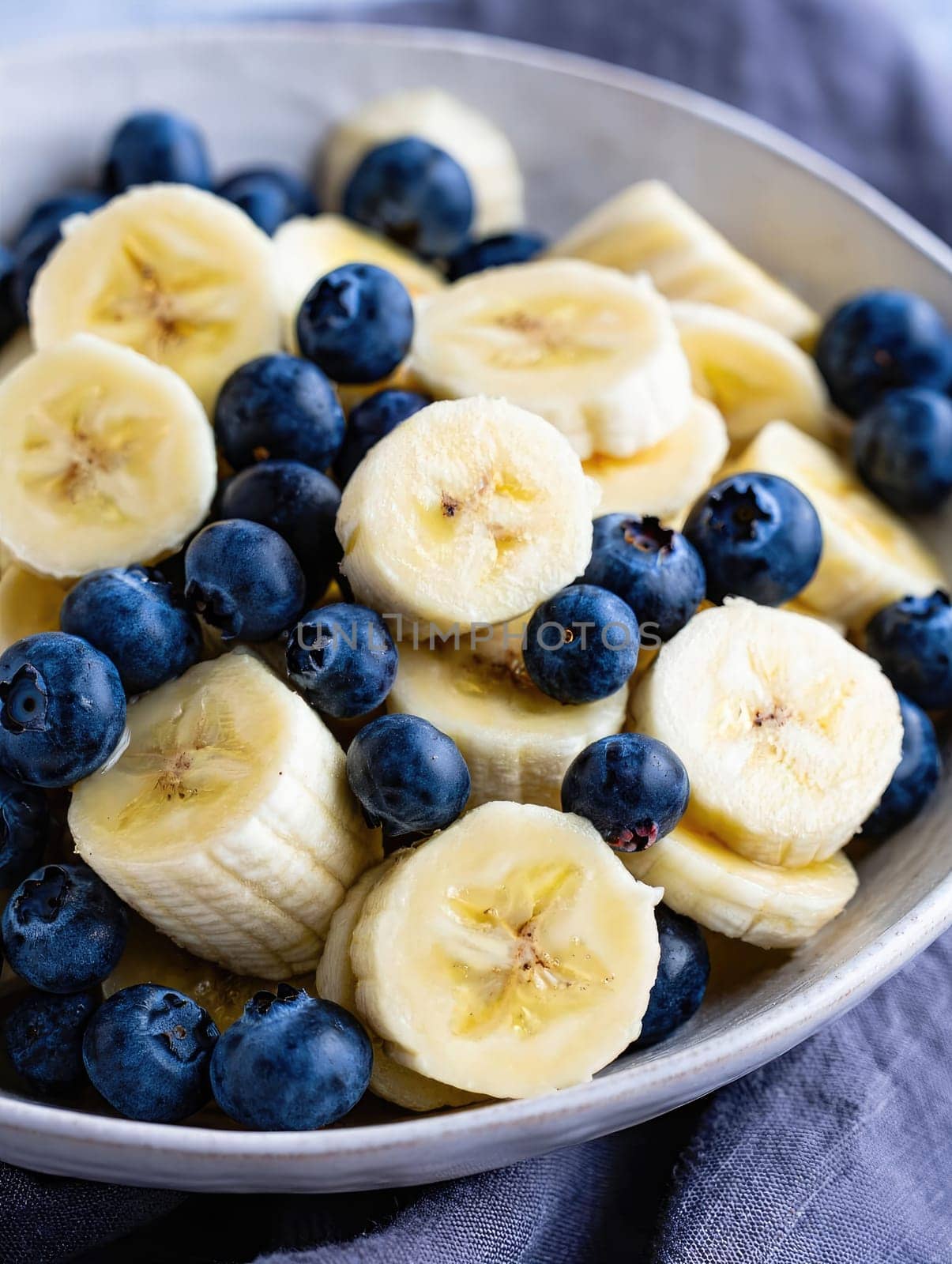 Slices of ripe banana are combined with plump blueberries in a bowl, creating a vibrant and healthy fruit salad. Ideal for a refreshing snack or breakfast option.