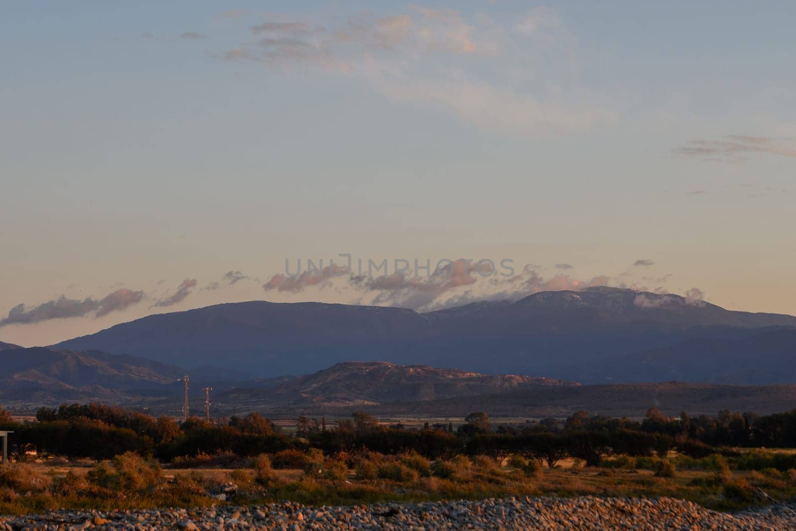 Twilight casts a warm glow over the majestic mountains, with wispy clouds drifting gracefully against the expansive sky. The valley below is tranquil, inviting reflection.