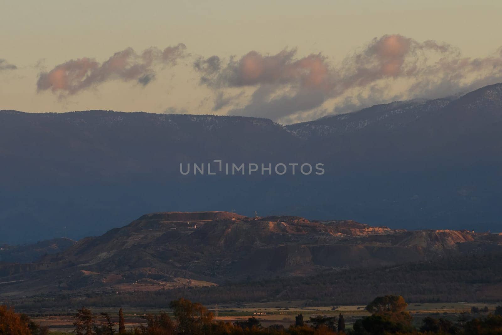 As dusk approaches, soft pastel clouds drift above the rugged peaks, creating a serene atmosphere over the expansive landscape filled with rolling hills and distant mountain ranges.