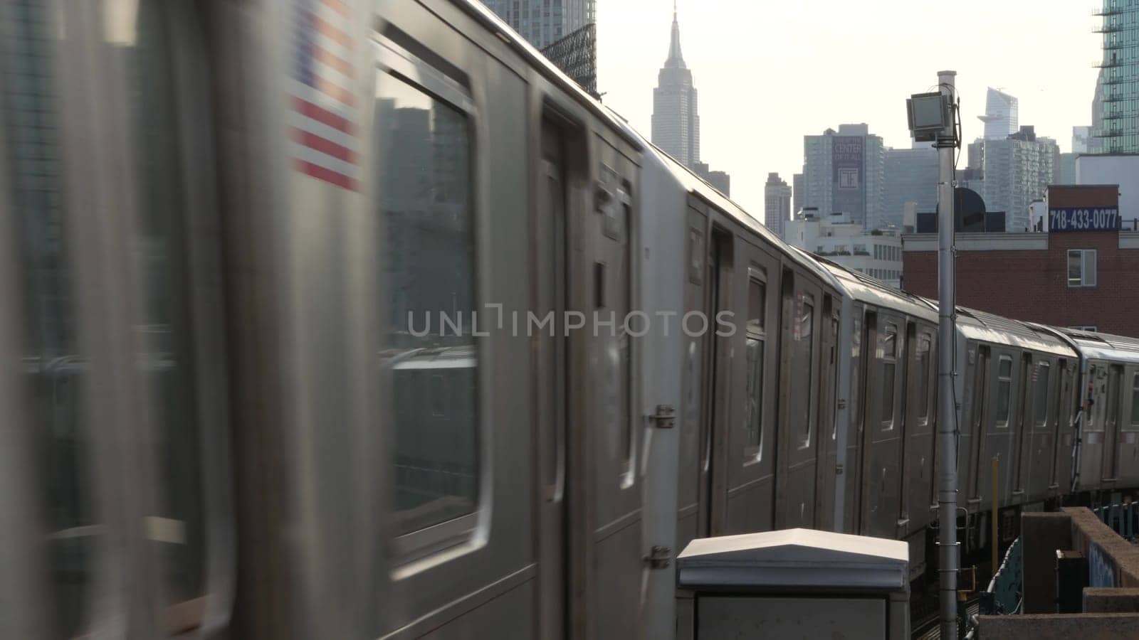 New York City, United States - 2 Sept 2023: Subway station. Metro train public transportation platform. Elevated outdoor railway, Queens passenger railroad traffic, Long Island. Empire State building.