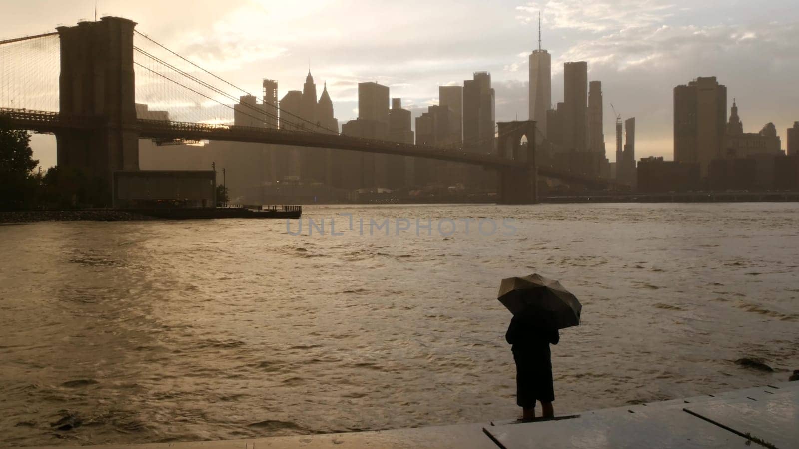 New York City, United States - 11 Sept 2023: Brooklyn Bridge rainy foggy day. Manhattan downtown skyline cityscape, World Trade Center. Man with umbrella, Dumbo Pebble Beach. Autumn river, fall in USA