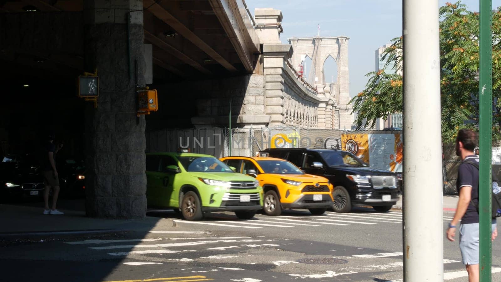 New York City, United States - 7 Sept 2023: Car on street road and Brooklyn Bridge to Manhattan downtown. Traffic on crossroad in Brooklyn under bridge. Yellow cab and green boro taxi. People crossing