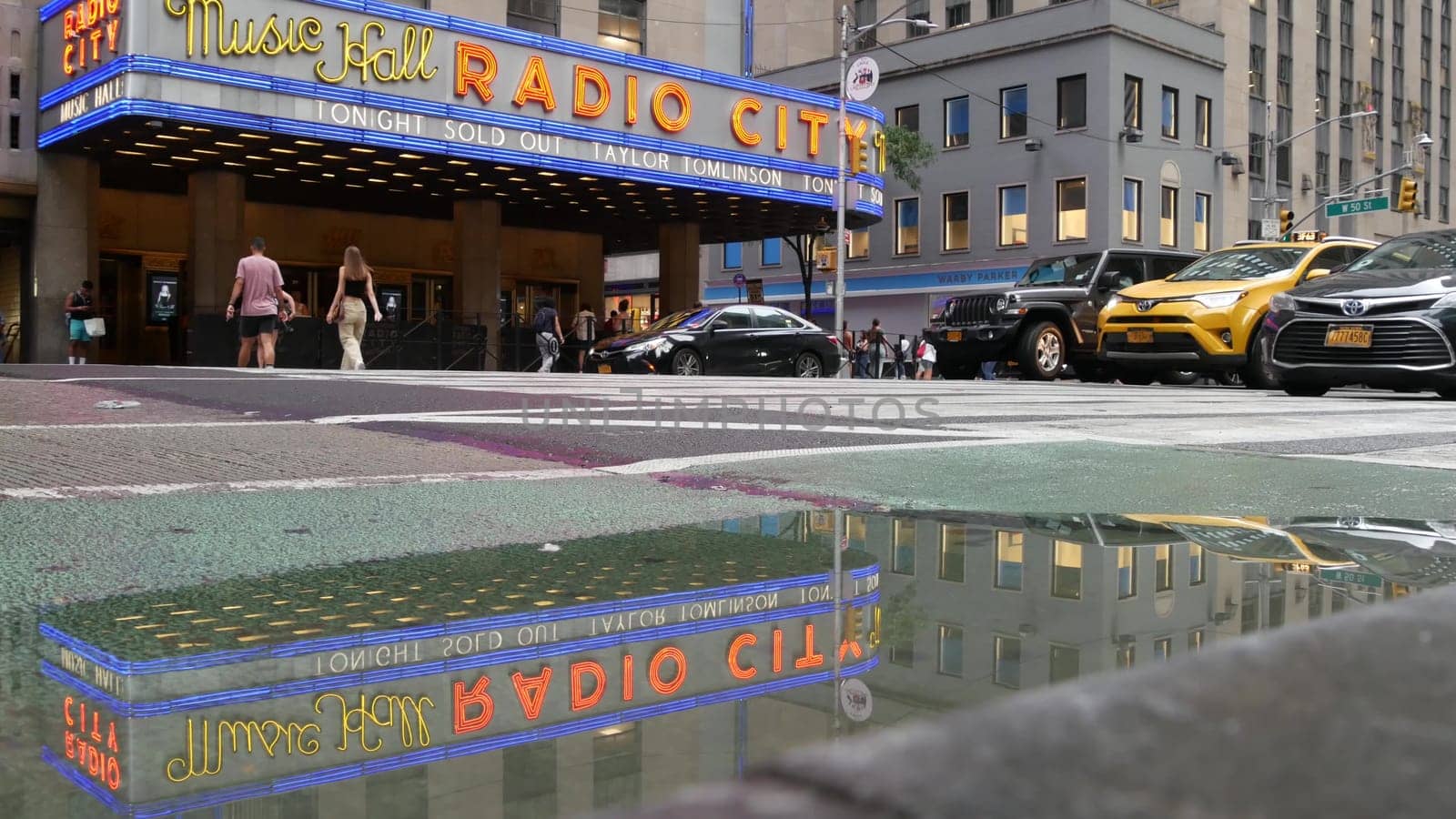 New York, United States - 10 Sept 2023: Manhattan Midtown street. Radio City Music Hall, Rockefeller Center, USA. People pedestrian, urban traffic, 6 Sixth Americas avenue crossroad, yellow taxi cab.
