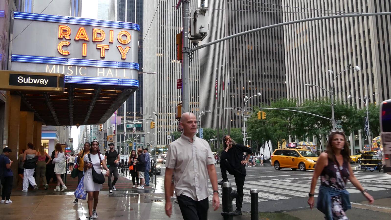 New York, United States - 10 Sept 2023: Manhattan Midtown street. Radio City Music Hall, Rockefeller Center, USA. People pedestrian, urban traffic, 6 Sixth Americas avenue crossroad, yellow taxi cab.