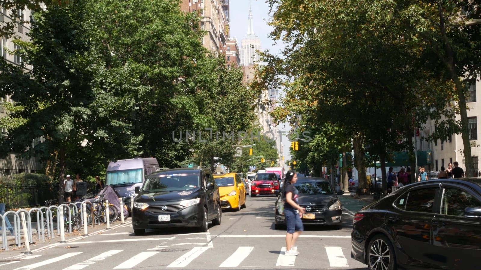 New York City, United States - 8 Sept 2023: Manhattan Greenwich Village street, 5th Fifth 5 avenue near Washington Square Park. American road car traffic, people. Yellow taxi cab, USA. Trees greenery.