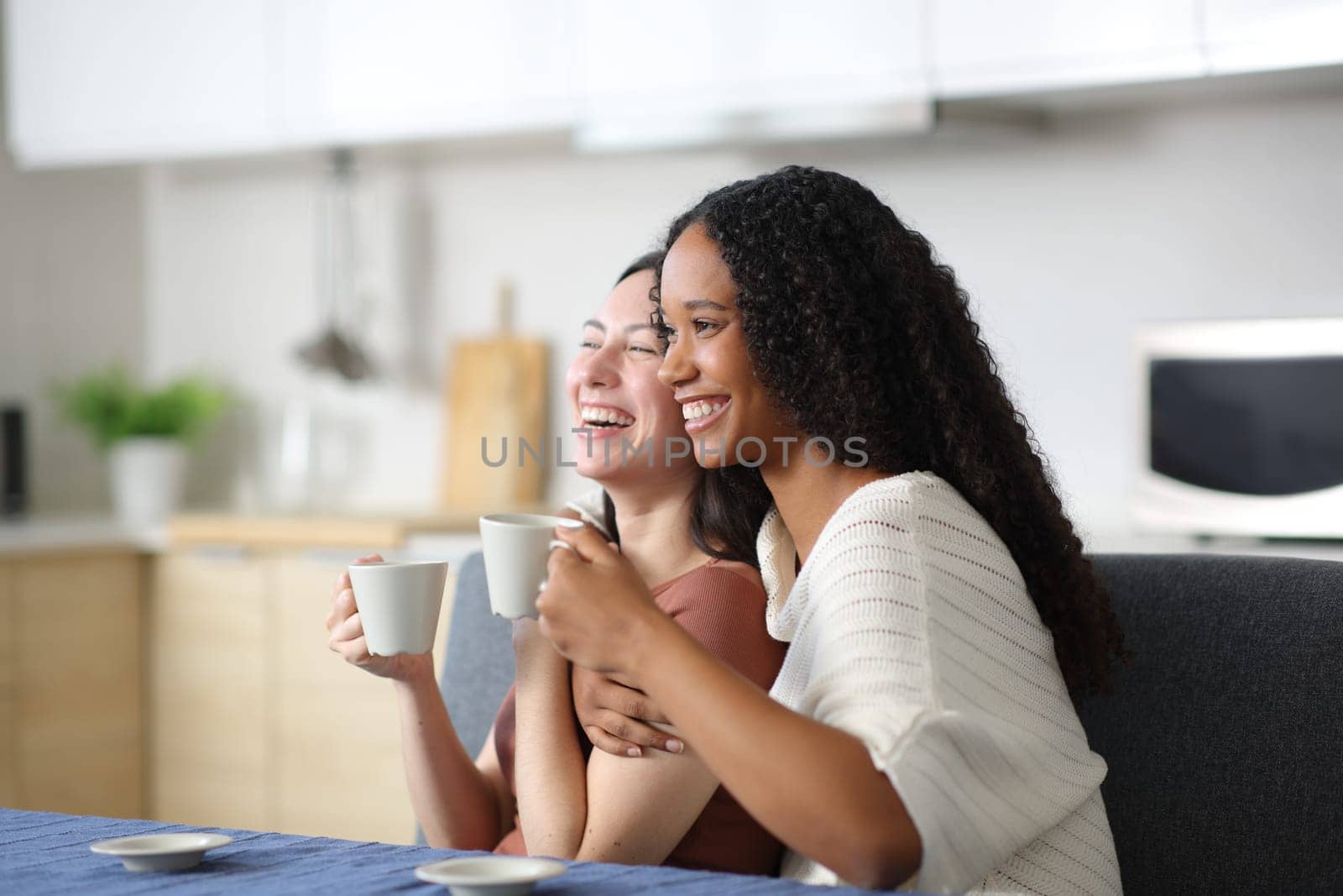 Happy interracial couple laughing drinking coffee in the kitchen at home