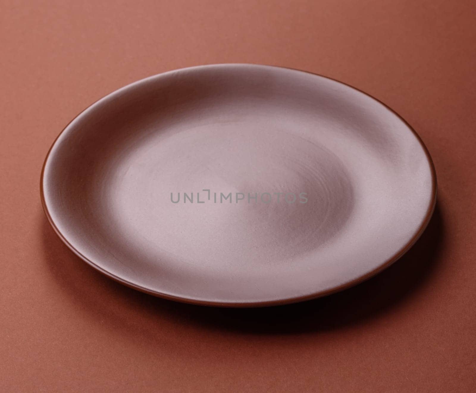 Empty ceramic plate on a monochrome brown background. Empty plate with cutlery on a dining table