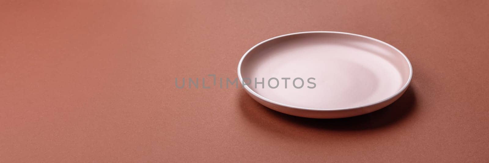 Empty ceramic plate on a monochrome brown background. Empty plate with cutlery on a dining table