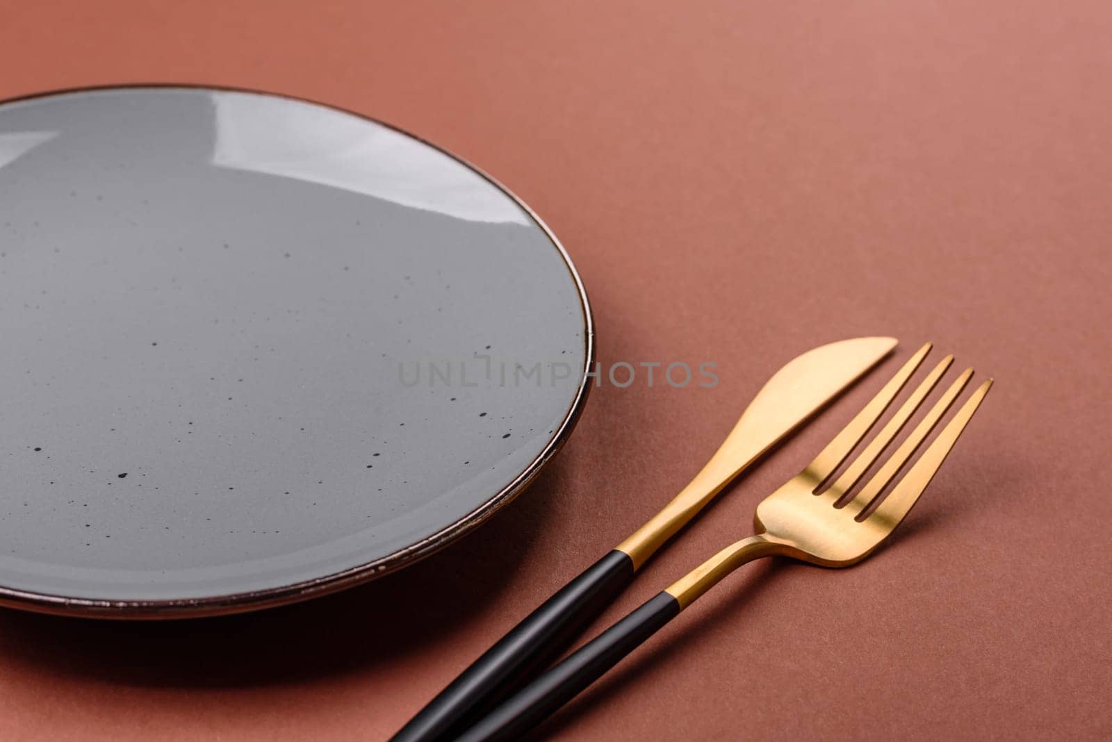 Empty ceramic plate on a monochrome brown background. Empty plate with cutlery on a dining table
