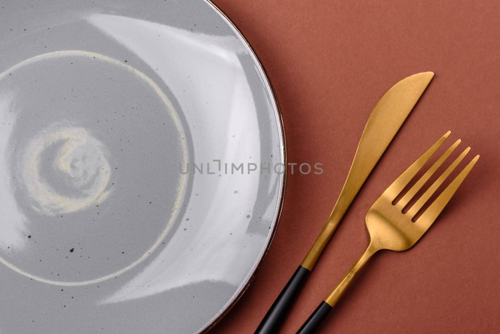 Empty ceramic plate on a monochrome brown background. Empty plate with cutlery on a dining table