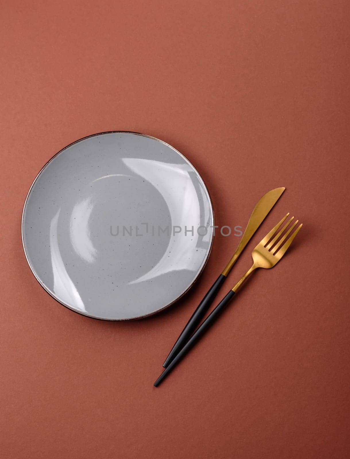 Empty ceramic plate on a monochrome brown background. Empty plate with cutlery on a dining table