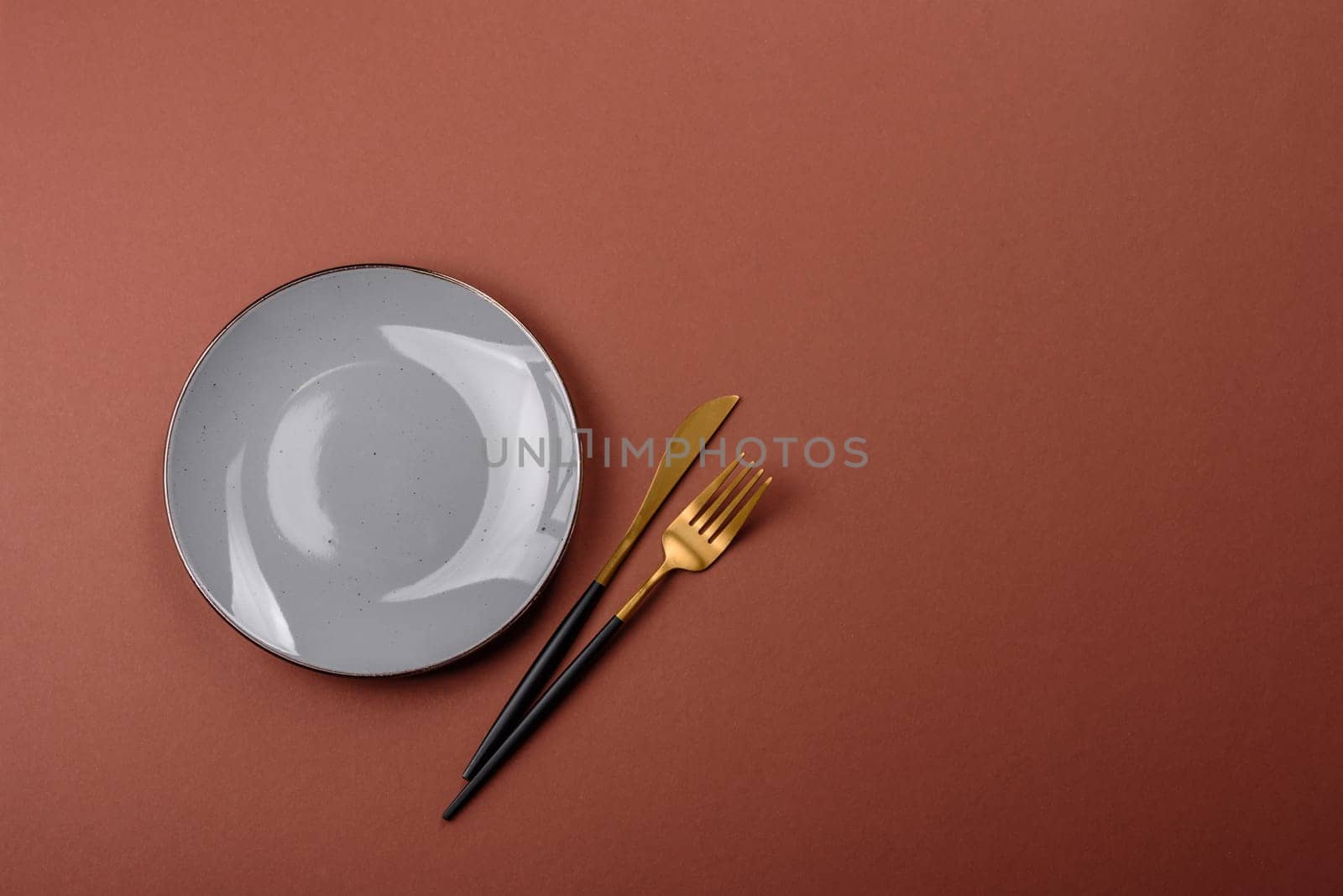Empty ceramic plate on a monochrome brown background. Empty plate with cutlery on a dining table