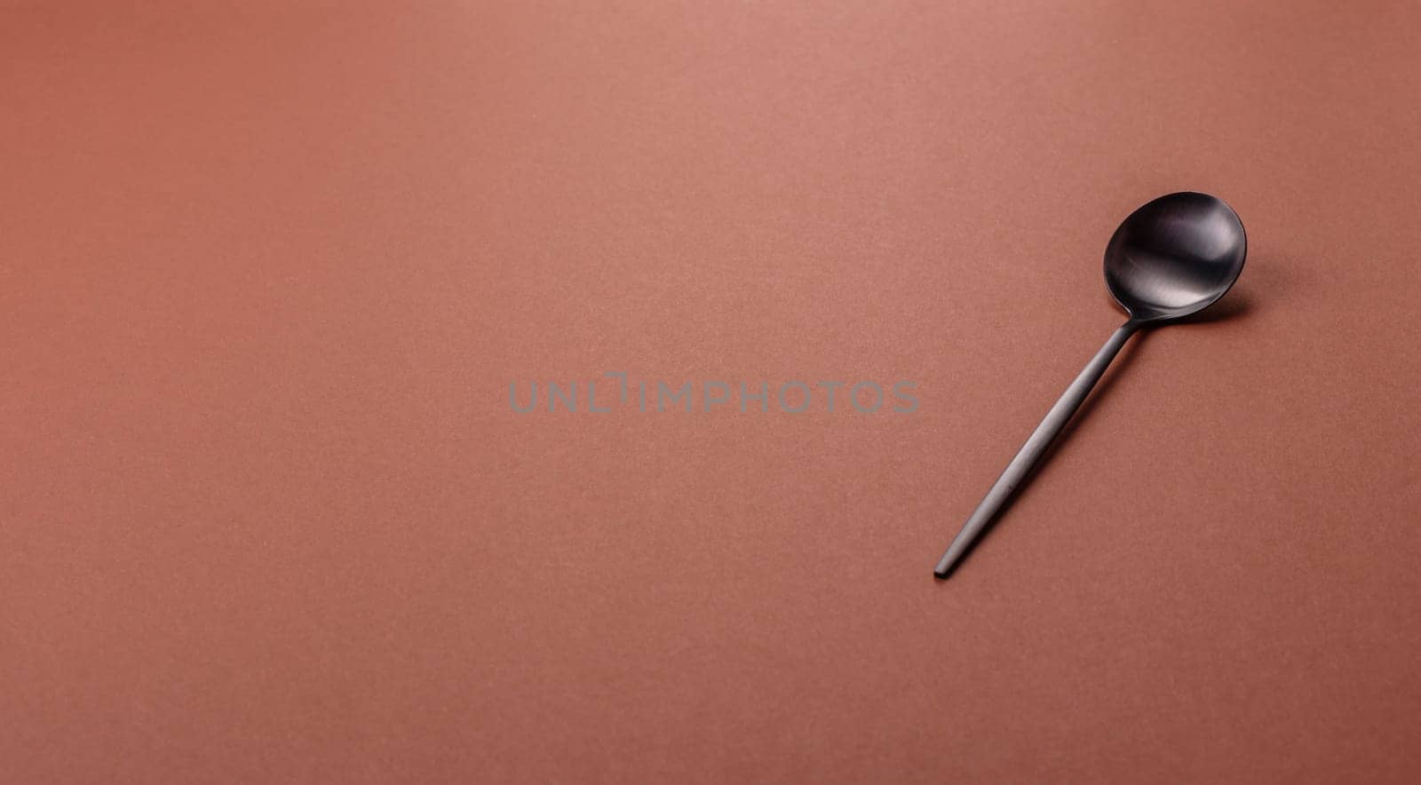 Empty metal spoon on a monochrome brown background. Cutlery on the dining table