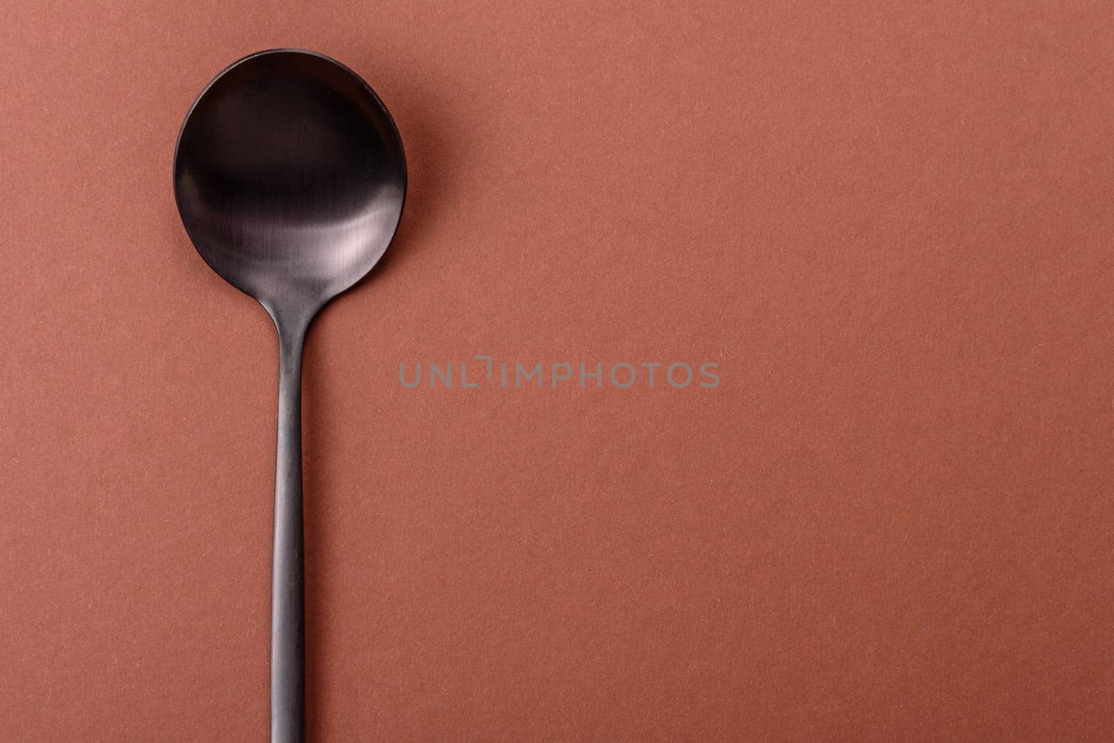 Empty metal spoon on a monochrome brown background. Cutlery on the dining table