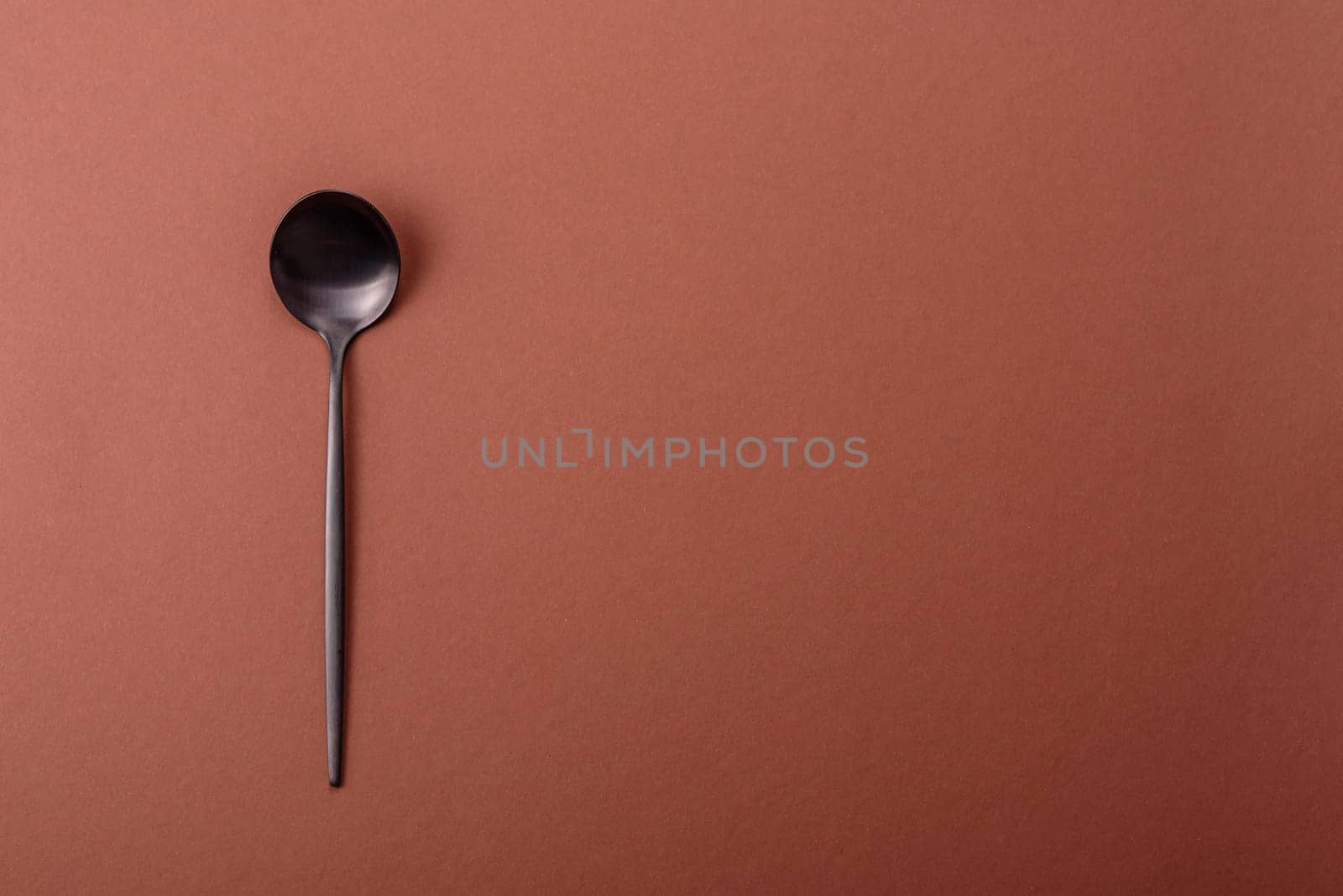 Empty metal spoon on a monochrome brown background. Cutlery on the dining table