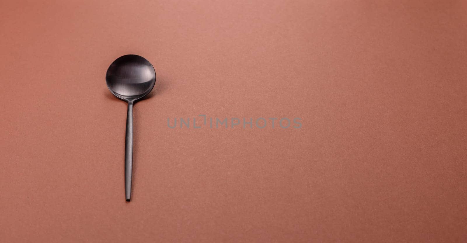 Empty metal spoon on a monochrome brown background. Cutlery on the dining table