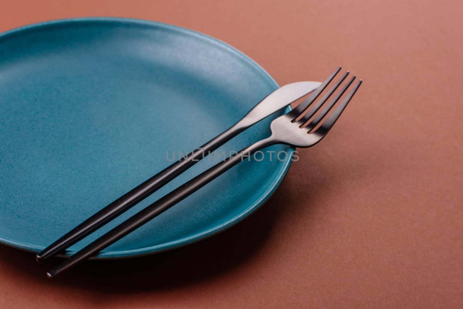 Empty ceramic plate on a monochrome brown background. Empty plate with cutlery on a dining table
