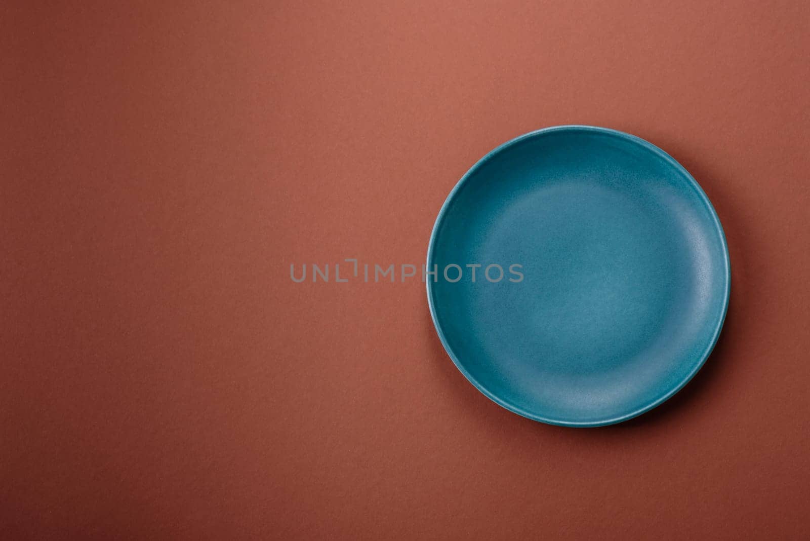 Empty ceramic plate on a monochrome brown background. Empty plate with cutlery on a dining table