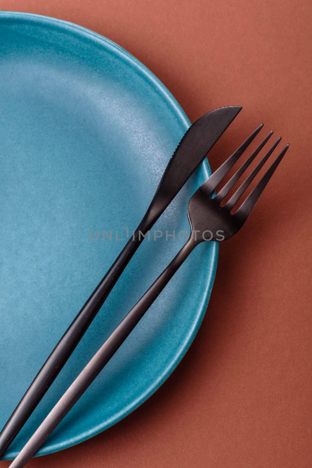 Empty ceramic plate on a monochrome brown background. Empty plate with cutlery on a dining table