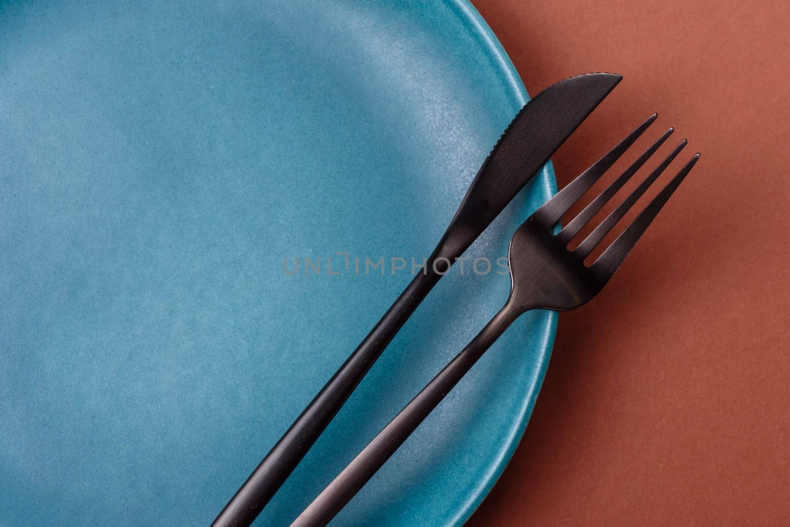 Empty ceramic plate on a monochrome brown background. Empty plate with cutlery on a dining table