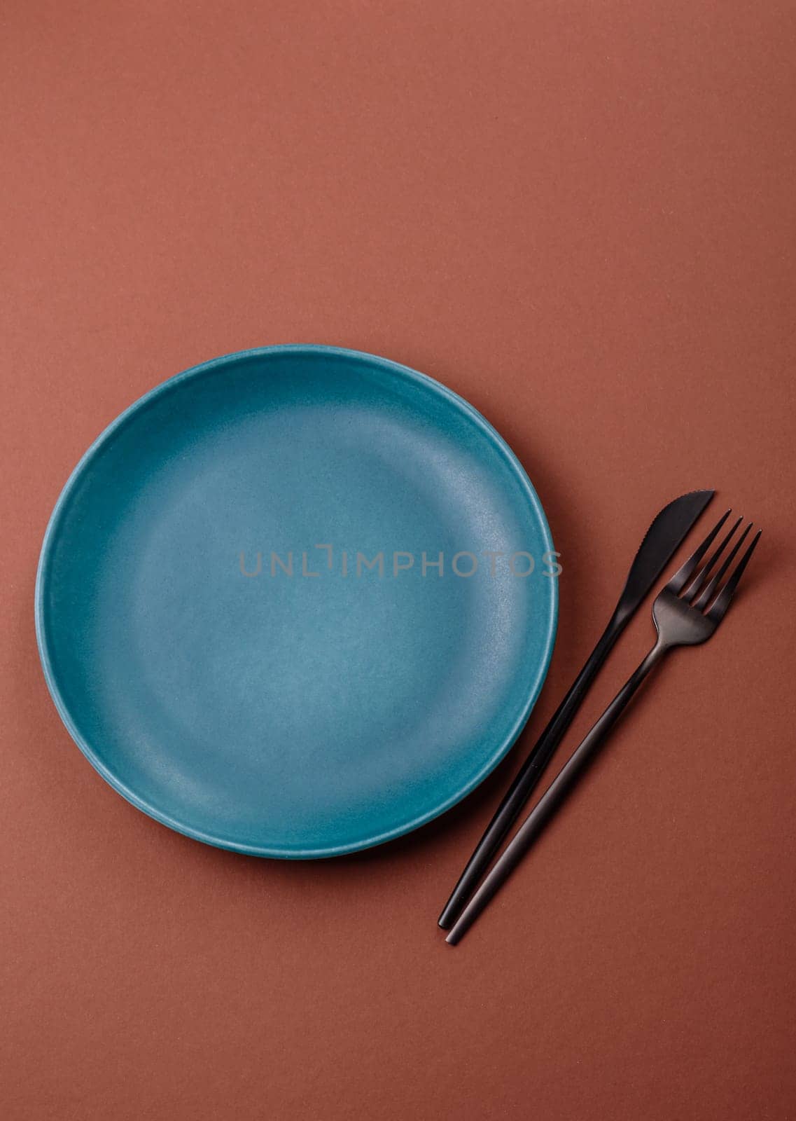 Empty ceramic plate on a monochrome brown background. Empty plate with cutlery on a dining table