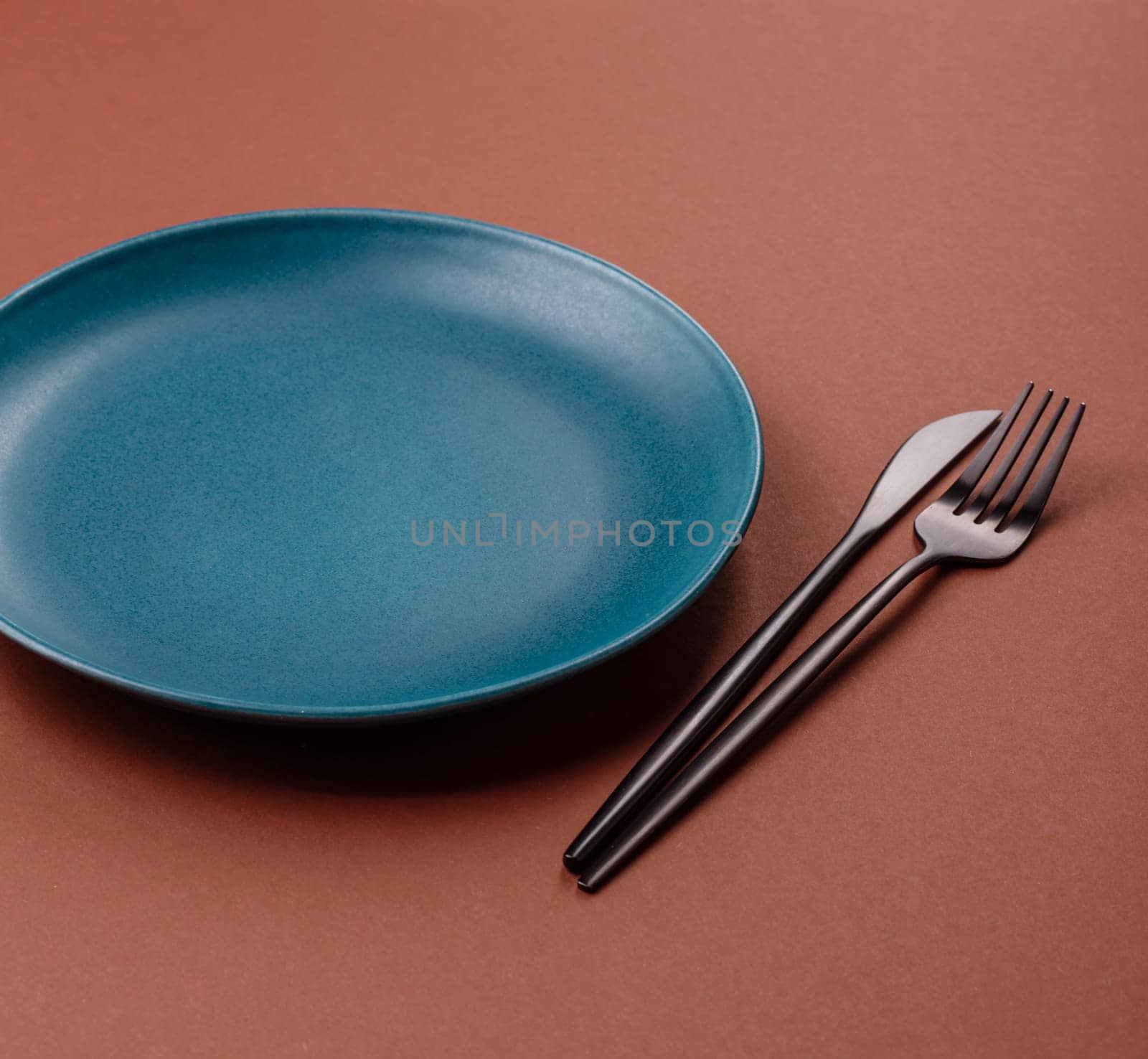 Empty ceramic plate on a monochrome brown background. Empty plate with cutlery on a dining table