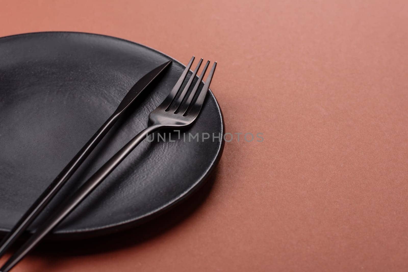 Empty ceramic plate on a monochrome brown background. Empty plate with cutlery on a dining table
