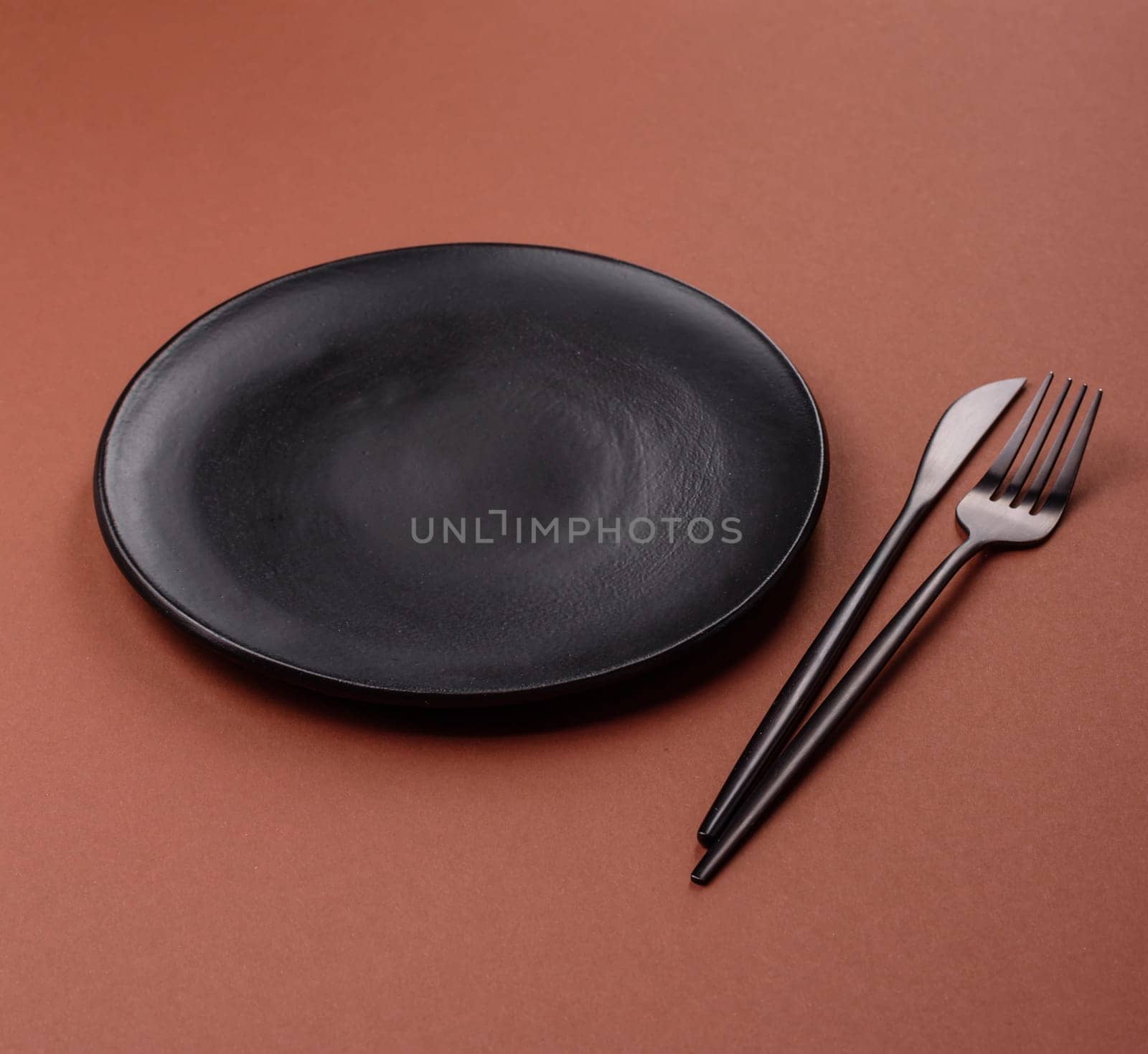 Empty ceramic plate on a monochrome brown background. Empty plate with cutlery on a dining table