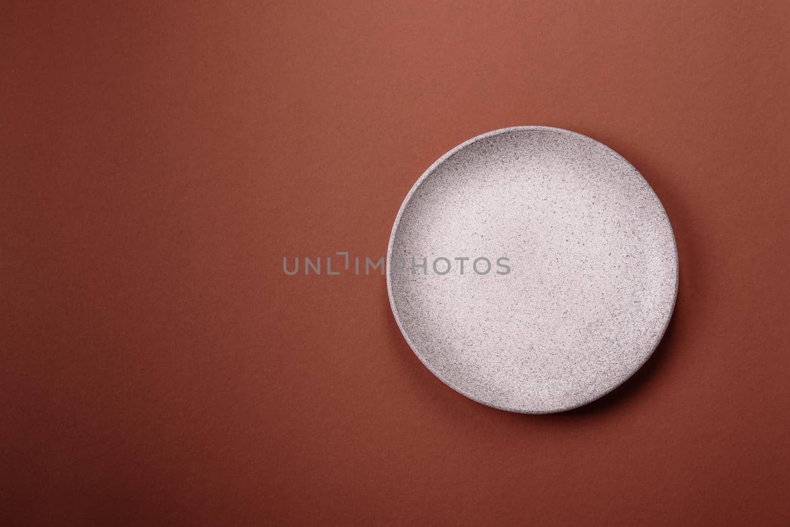 Empty ceramic plate on a monochrome brown background. Empty plate with cutlery on a dining table