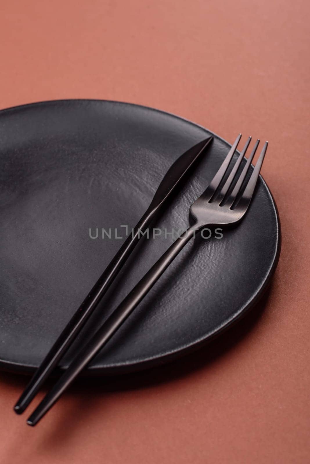 Empty ceramic plate on a monochrome brown background. Empty plate with cutlery on a dining table