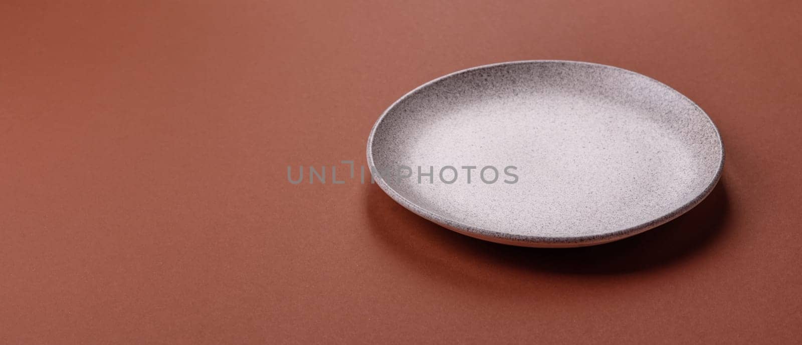 Empty ceramic plate on a monochrome brown background. Empty plate with cutlery on a dining table