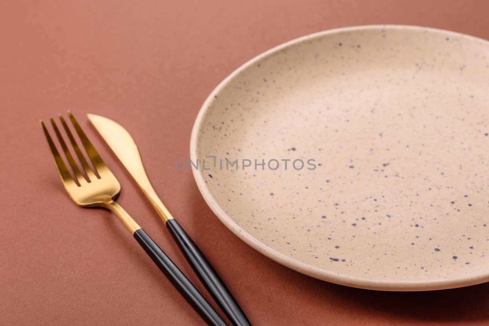 Empty ceramic plate on a monochrome brown background. Empty plate with cutlery on a dining table