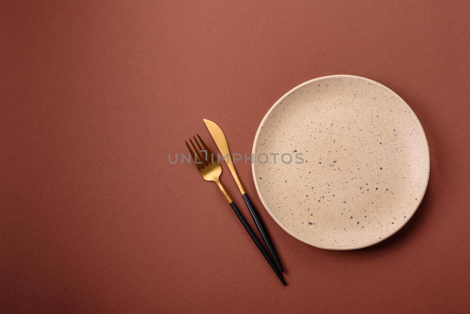 Empty ceramic plate on a monochrome brown background. Empty plate with cutlery on a dining table