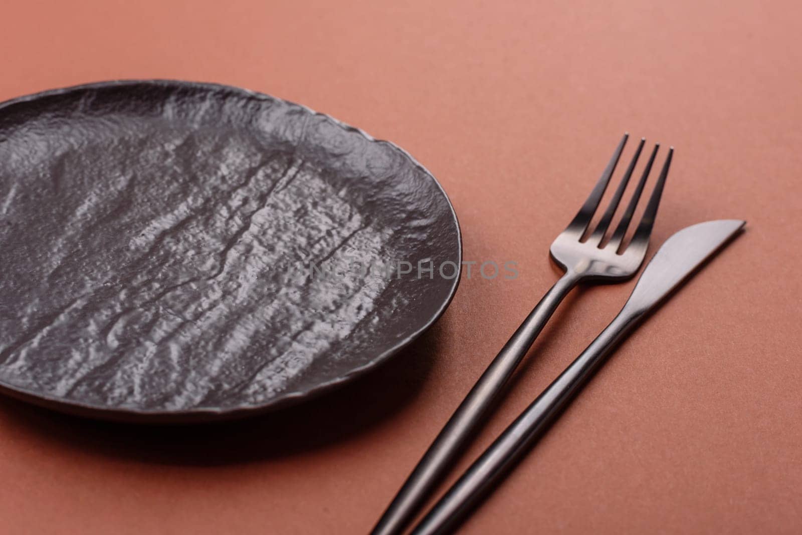 Empty ceramic plate on a monochrome brown background. Empty plate with cutlery on a dining table