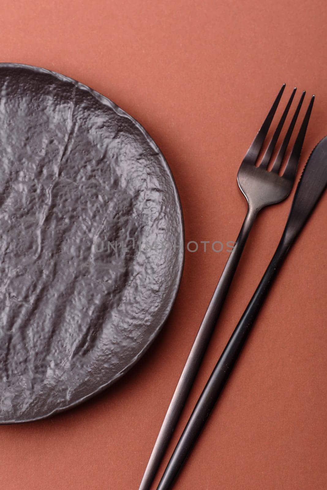 Empty ceramic plate on a monochrome brown background. Empty plate with cutlery on a dining table