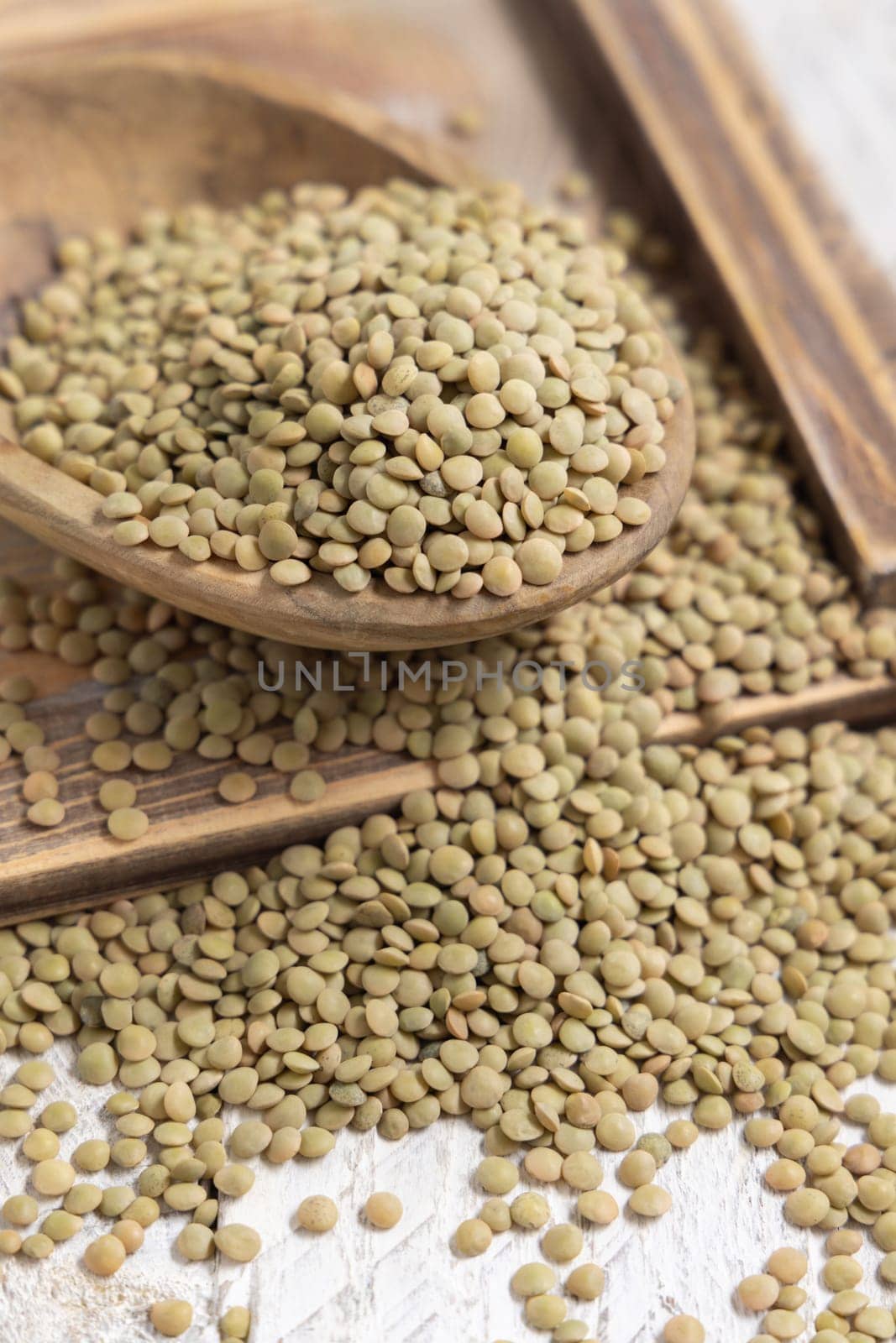 Wooden bowl full of dried raw green lentils on white table close up. Healthy raw vegetarian food, legumes plant-based protein source. Traditional mediterranean ingredient