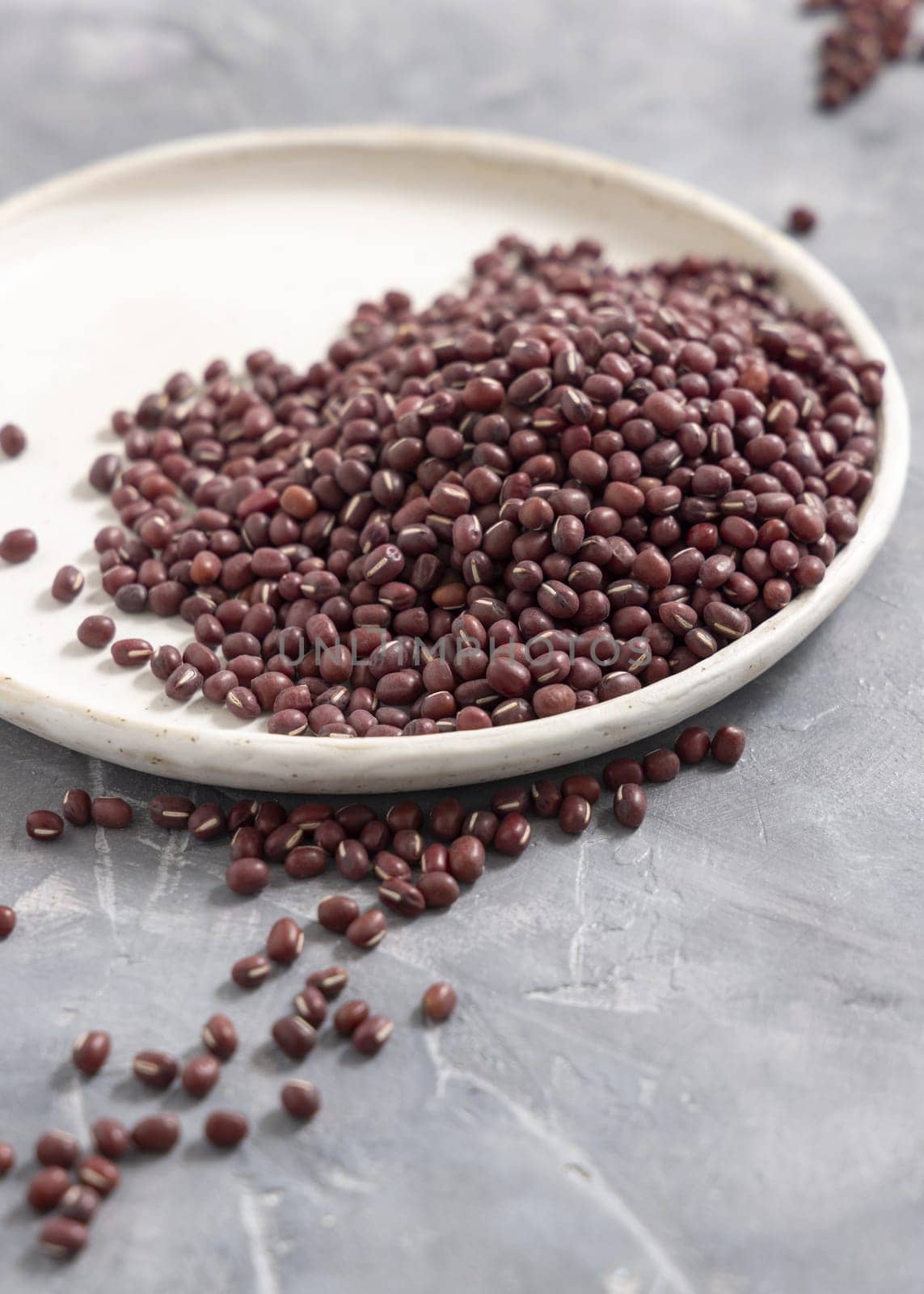Ceramic plate full of dried red azuki beans on gray table closeup, copy space. Healthy vegetarian food, legumes protein source. Traditional East Asiancousin ingredient