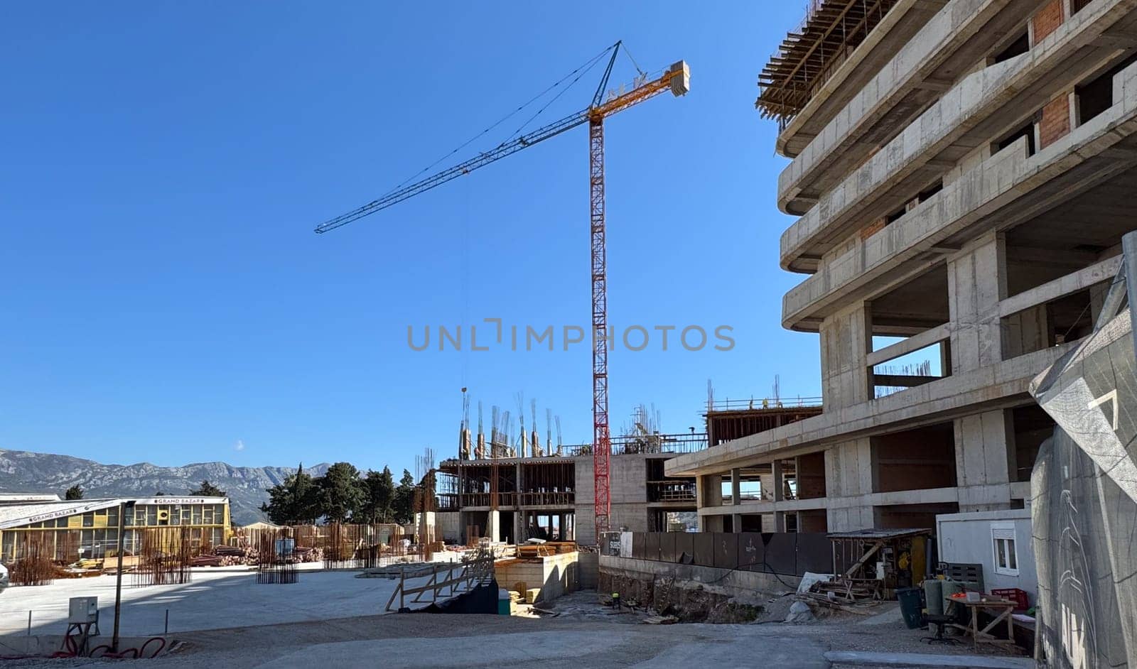 Budva,Montenegro-April 11,2025:A construction site with a tower crane and partially built multi-story concrete structure under a clear blue sky.