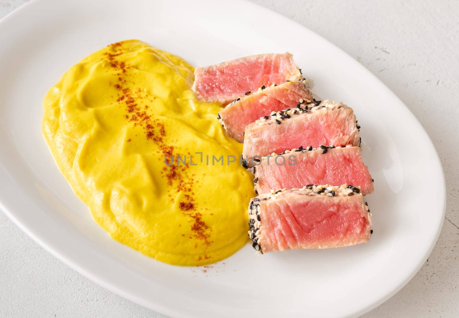 Crisp sesame tuna rests beside smooth cauliflower curry, balanced and visually refined